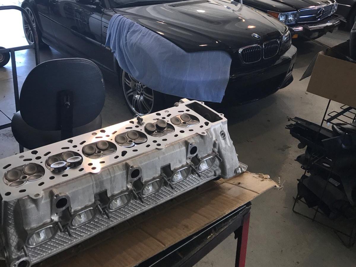 Cylinder head on a workbench in front of a BMW M3 and a Mercedes-Benz SL at Auto Star Co.